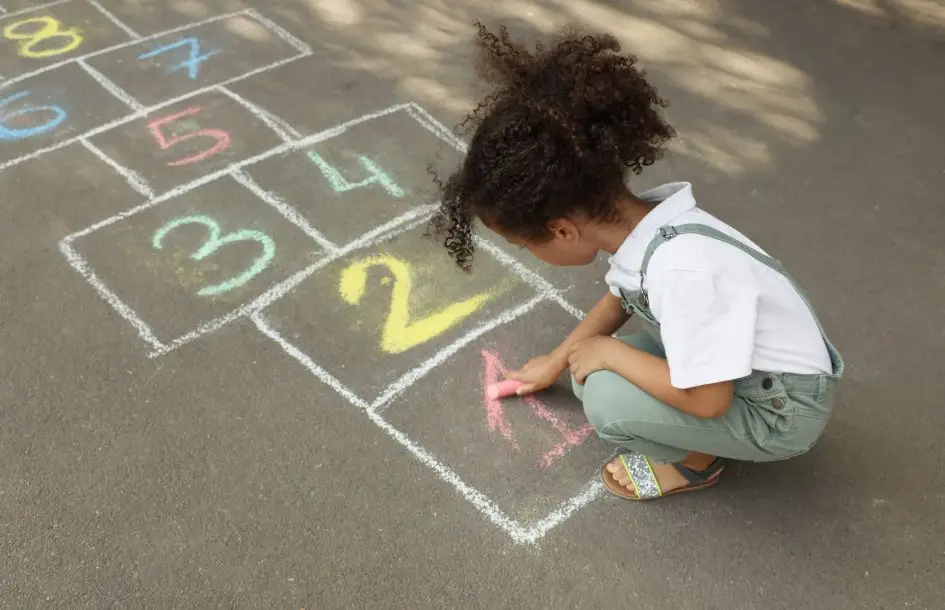 girl drawing hopscotch with chalk on asphalt outdoors, supporting early math skills for preschoolers through play