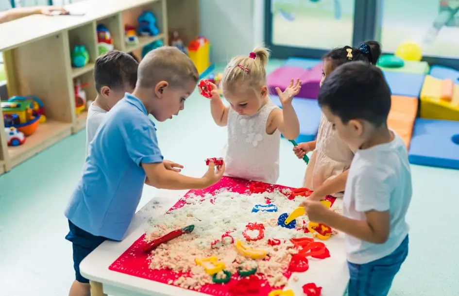 Early socialization in early childhood, kids surrounded kinetic sand table playing