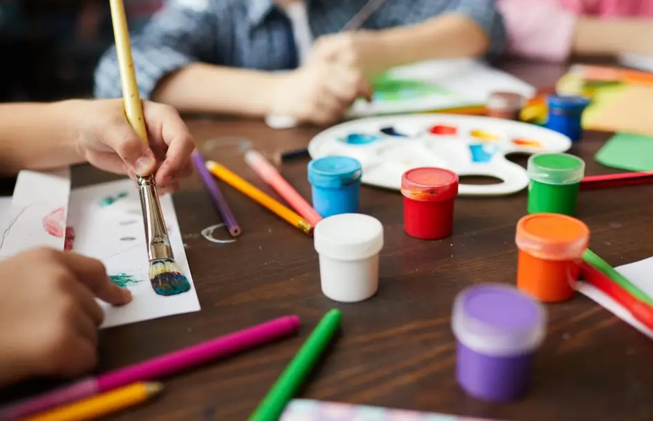 Closeup of children painting pictures, focus on art supplies paints, pencils and crayons, copy space open ended play