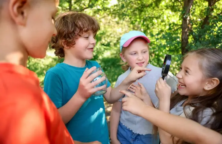 Children with magnifying glass and jar in nature doing nature scavenger hunt for kids