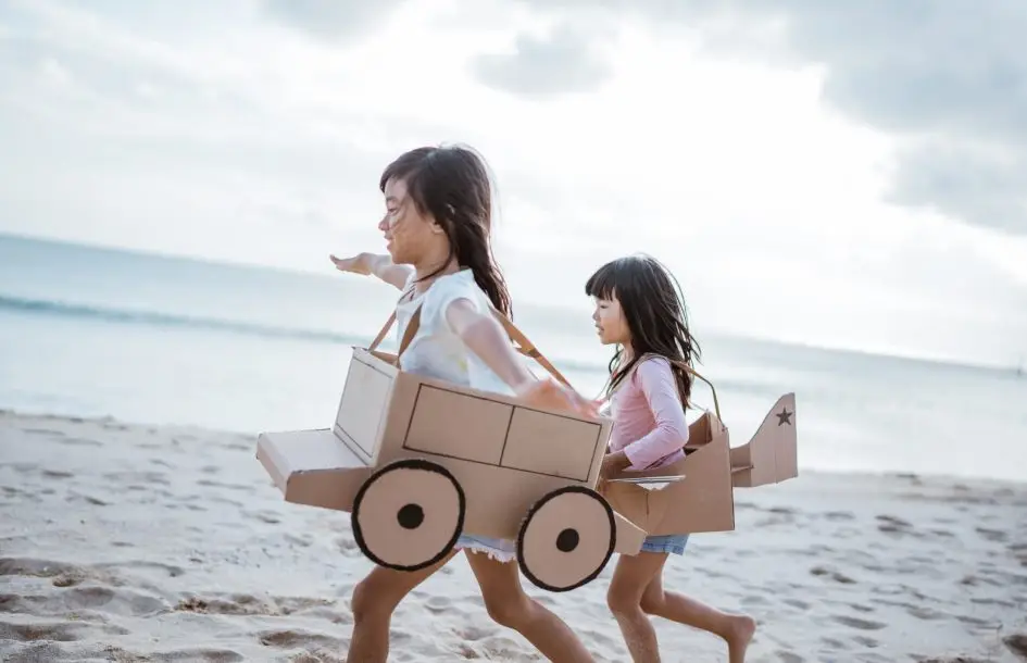 sibling and girl friend playing with cardboard airplane and car on the beach, summer stem activities of kids