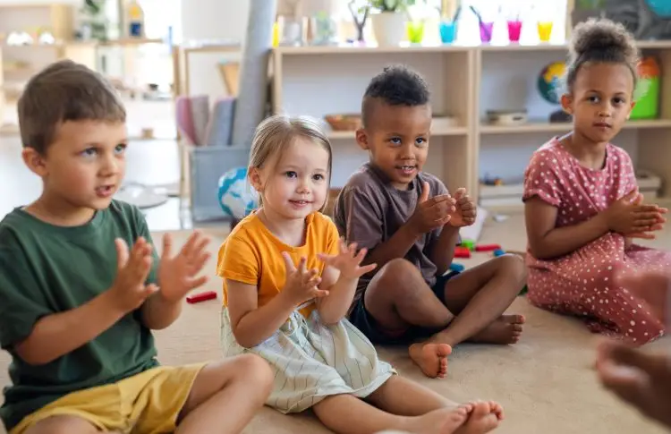 Group of small nursery school children sitting on floor indoors in classroom, clapping. for rhyming and leter games, early reading activities for kids